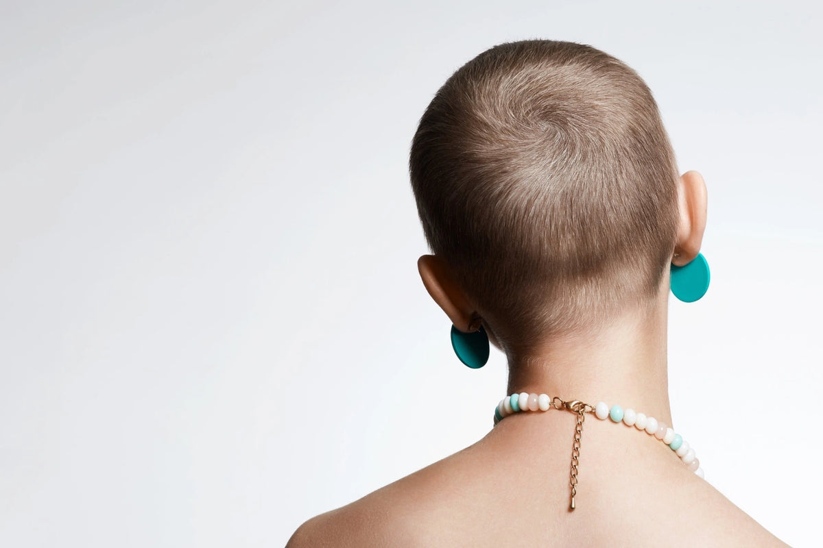 Femme avec les cheveux rasés en préparation de traitements de chimiothérapie de dos avec des bijoux