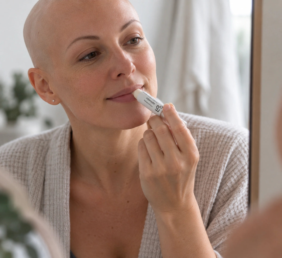 Femme vivant avec une perte de cheveux du au cancer ou à la chimiothérapie en train de s'appliquer un baume à lèvres