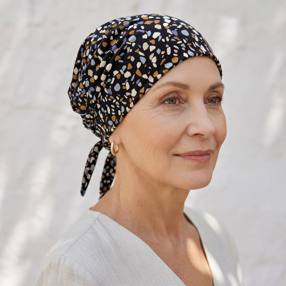 Femme vivant avec une perte de cheveux du au cancer ou à la chimiothérapie avec un foulard rétro eéclats Sibelle à l'extérieur