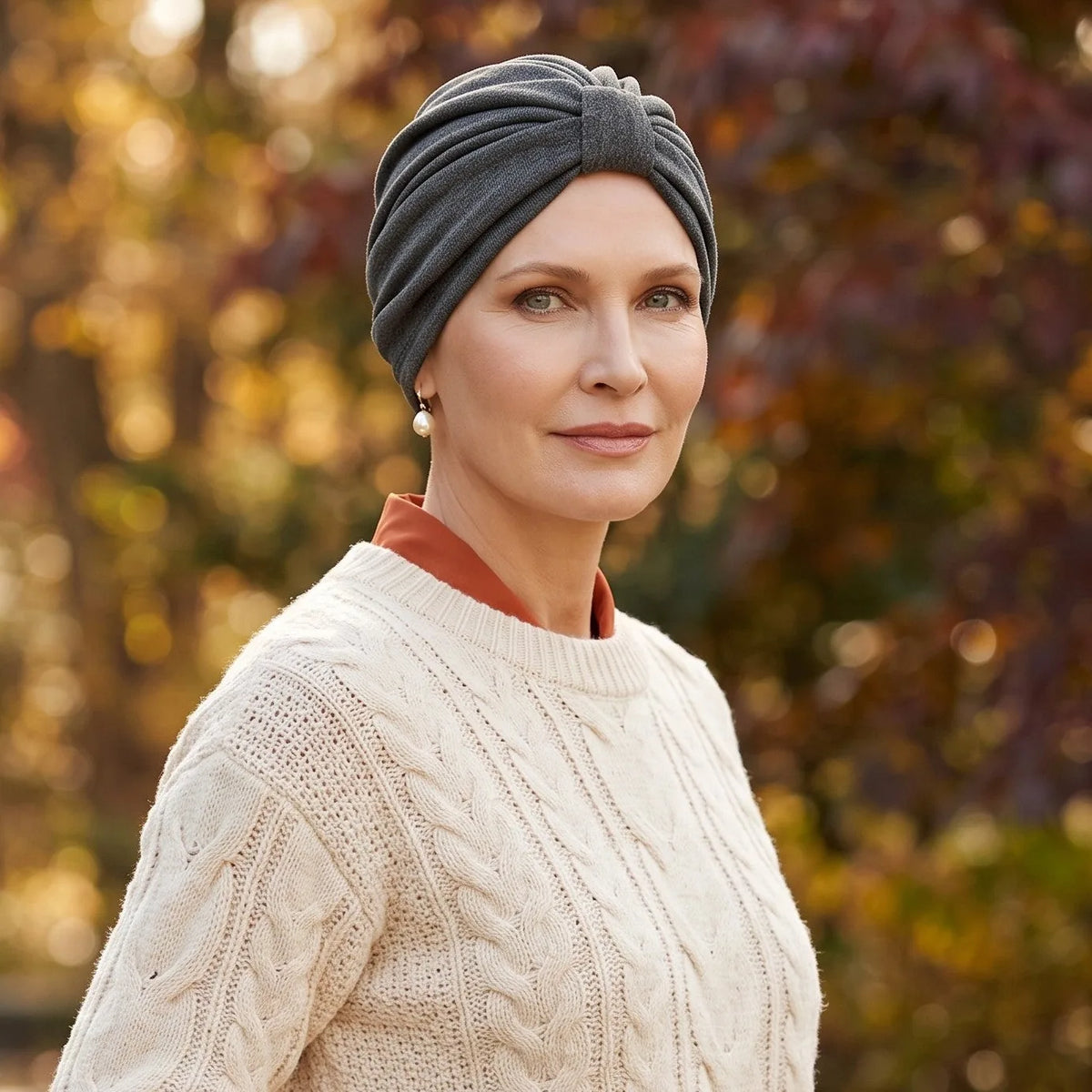 Femme vivant avec une perte de cheveux du au cancer ou à la chimiothérapie avec un turban urbain en tricot vert Sibelle dans un parc l'automne